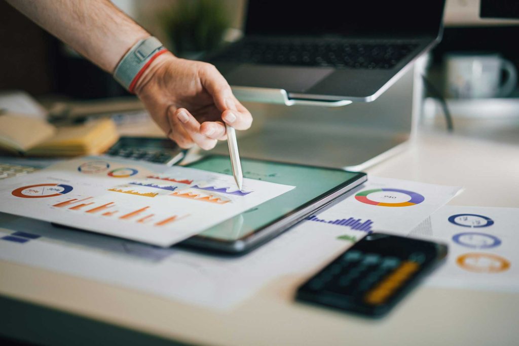 Osoba analyzuje grafy a finanční zprávy na tabletu a dokumentech.